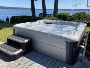 A Hot Spring Envoy hot tub is pictured in a customer's yard in Bremerton, with two steps and a body of water in the background.